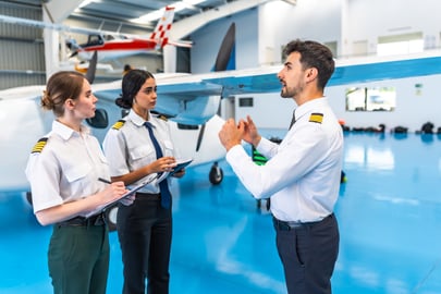 Flight instructor briefing two pilots beside an aircraft in a hangar