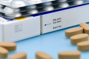 Close‑up of medication packaging showing manufacture date, expiry date, and batch number, with tablets placed nearby to highlight medication shelf life and compliance